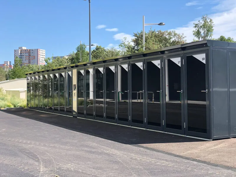 Reihe moderner, verschließbarer Fahrradboxen mit glatten dunklen Türen und digitalem Zugangssystem, aufgestellt entlang einer Wohnanlage in der Ödenburgerstraße